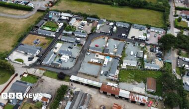 An aerial view of lots of caravans and static homes on brownfield land, surrounded by green fields.