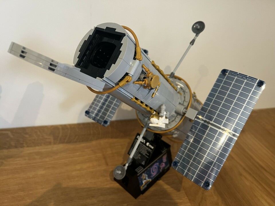 Lego Hubble Space Telescope model with open panels on a stand against a plain wall.