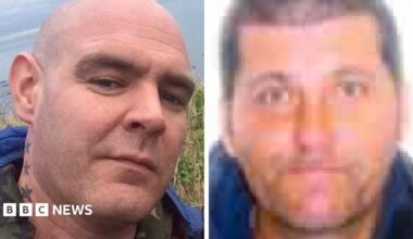 Two men side by side. They are in close up. The man on the left is bald with stars tattooed on his neck. The man on the right has dark hair.