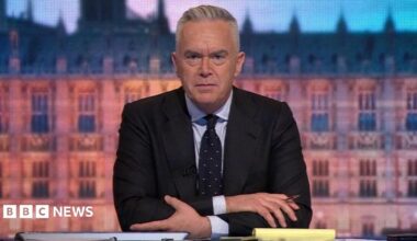Huw Edwards, who has grey hair, wearing a dark jacket and blue tie over a light shirt