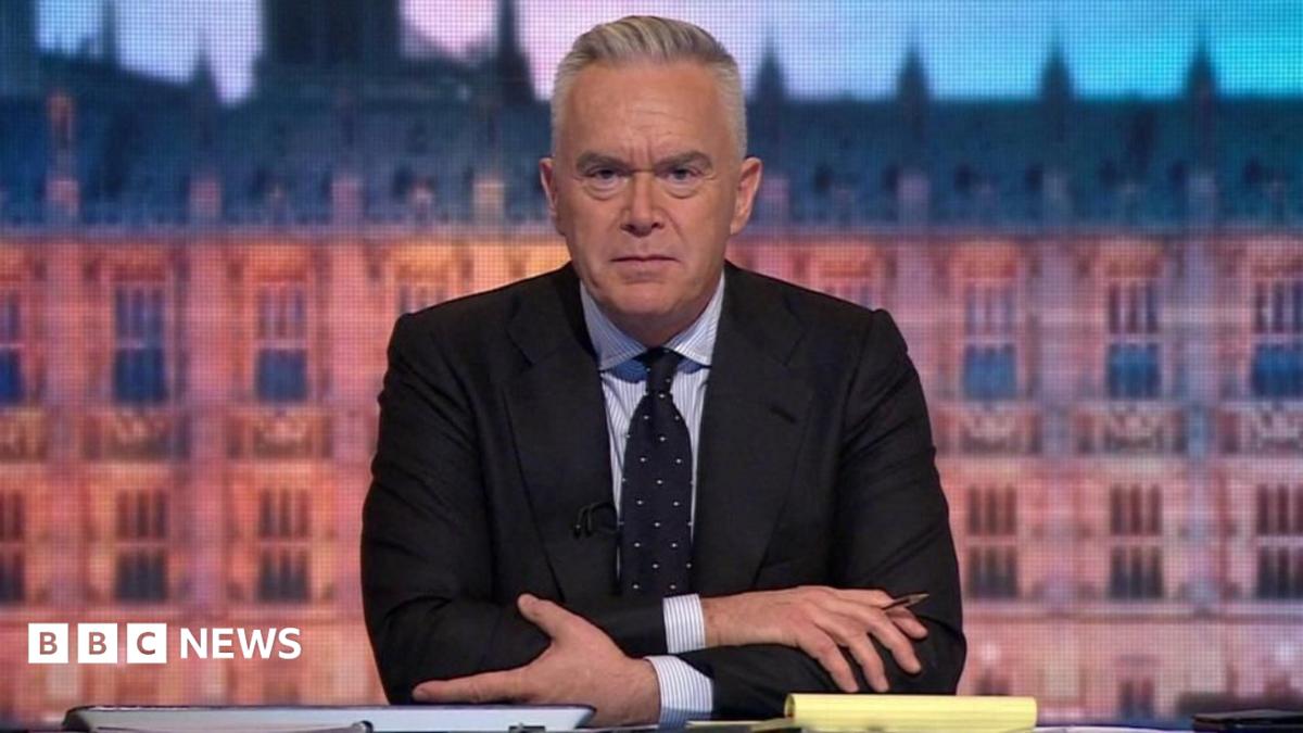 Huw Edwards, who has grey hair, wearing a dark jacket and blue tie over a light shirt