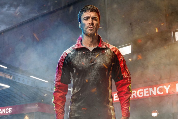 Olly Rix as Flynn Byron, covered in dust and stood outside of the hospital from Casualty