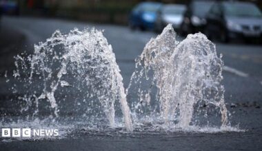 Water spurts upwards out of a drain on a road.