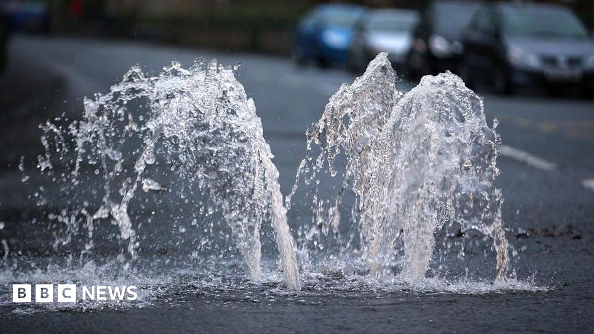 Water spurts upwards out of a drain on a road.