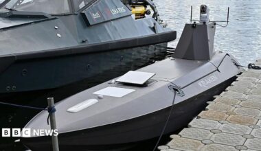 A Kraken K3 Scout high-performance USV drone parked next to a larger boat with water shown behind it