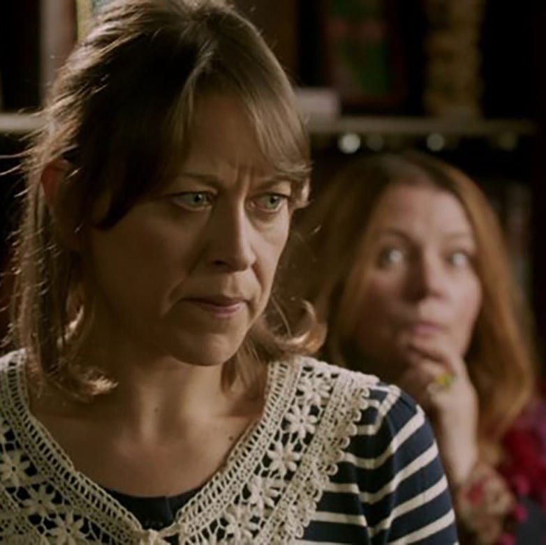 two women indoors, one in focus looking serious, the other blurred in the background. two women indoors, one in focus looking serious, the other blurred in the background.