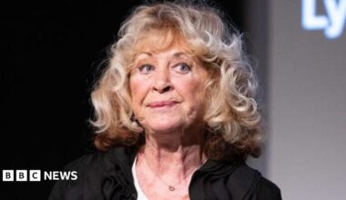 La Plante pictured at an event in 2021, looking away from the camera with a pensive expression on her face, wearing a black top and big blonde curls.