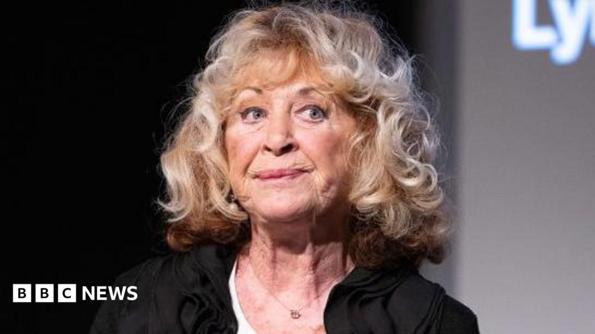 La Plante pictured at an event in 2021, looking away from the camera with a pensive expression on her face, wearing a black top and big blonde curls.