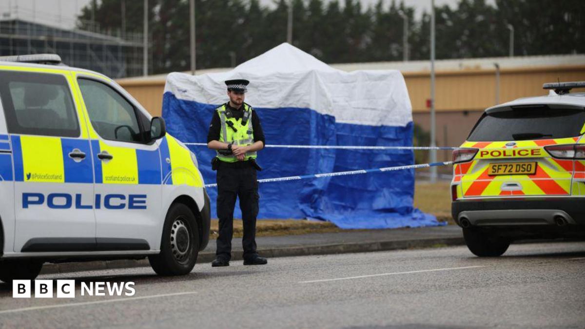 A police officer standing in front of a police cordon and blue forensic tent and two police vehicles in Arbroath.