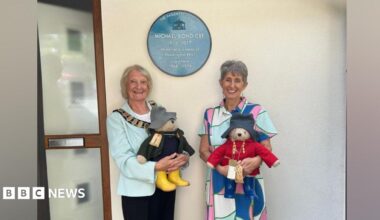 On the right is Karen Jankel, the daughter of Paddington Bear author Michael Bond, pictured at the unveiling with a Paddington Bear. She is wearing a patterned dress and has grey hair. On the left is Haslemere mayor Jacquie Keen, who is also holding a Paddington Bear and is wearing a light green jacket and black trousers. She has blonde hair.