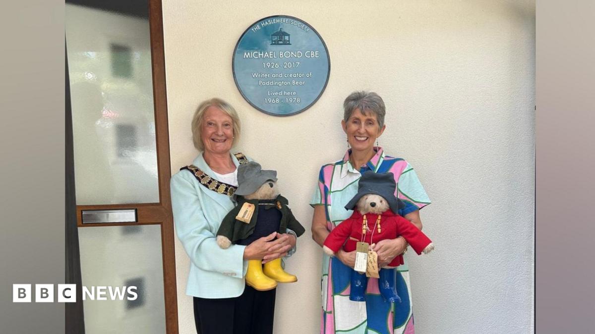 On the right is Karen Jankel, the daughter of Paddington Bear author Michael Bond, pictured at the unveiling with a Paddington Bear. She is wearing a patterned dress and has grey hair. On the left is Haslemere mayor Jacquie Keen, who is also holding a Paddington Bear and is wearing a light green jacket and black trousers. She has blonde hair.