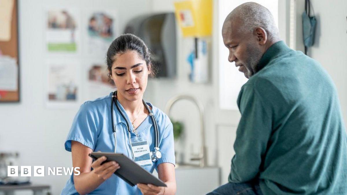 A nurse in blue scrubs with a stethoscope consults with a Black patient in a clinic, using a tablet. Warm, professional healthcare scene highlighting patient care and medical teamwork.
