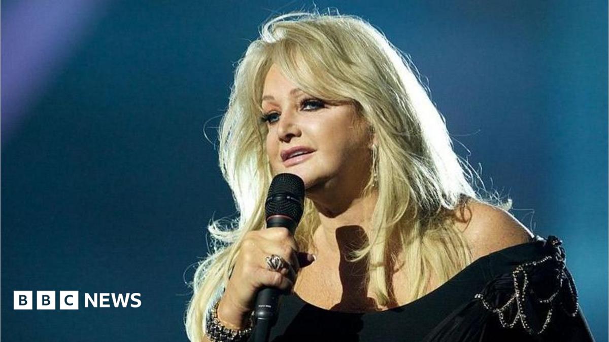 Bonnie Tyler, wearing a black dress, can be seen singing on stage
