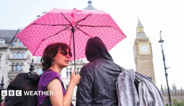 Two people stand under a pink umbrella sheltering from the rain with the Westminster skyline in the background