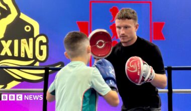 Boxer Dalton Smith wears pads on his hands as he coaches a young boxer in the ring.