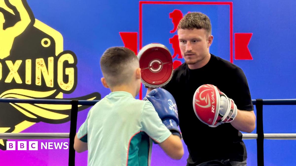 Boxer Dalton Smith wears pads on his hands as he coaches a young boxer in the ring.