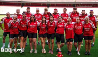 A group of people wearing arsenal t shirts posing pitch-side at the emirates stadium in London