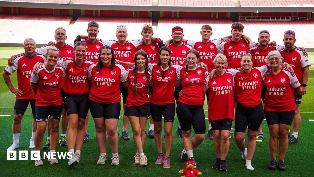 A group of people wearing arsenal t shirts posing pitch-side at the emirates stadium in London