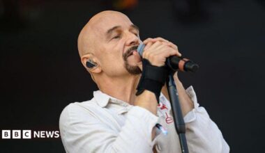 A bald man with a goatee singing into a microphone