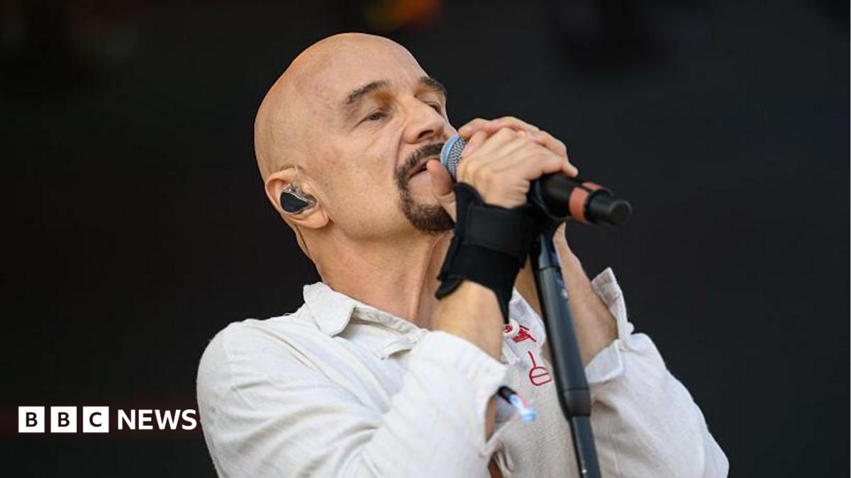 A bald man with a goatee singing into a microphone