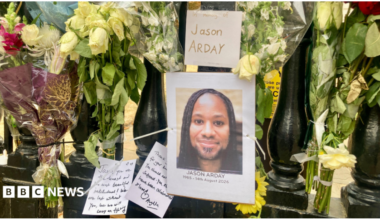 Floral tributes attached to black railings. There is a picture of Jason Arday, with notes written to him.