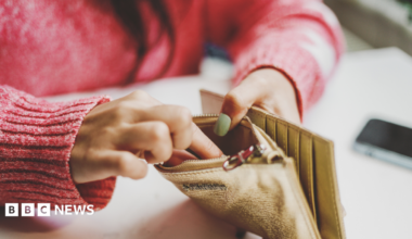 Person with red jumper has fingers inside gold coloured wallet.
