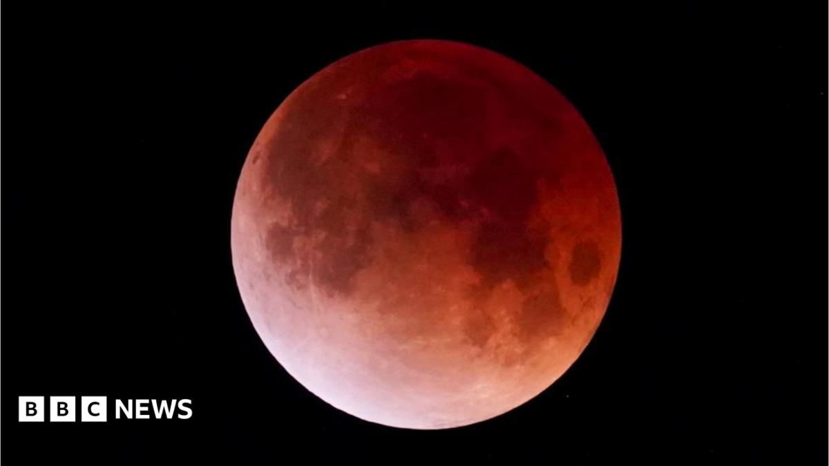 An image of the moon during a partial lunar eclipse shows it in a shade of red, caused by the lack of light hitting its surface. It is surrounded by the black openness of space.