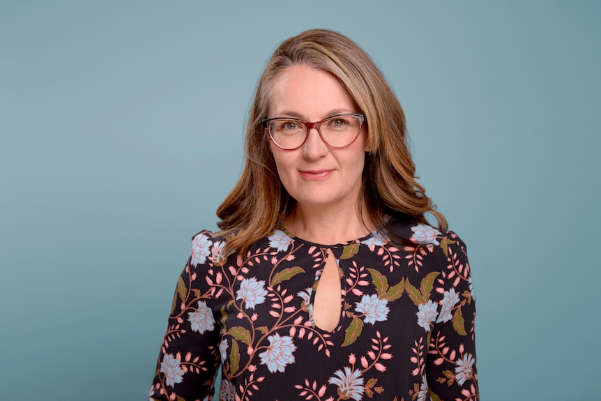 Judy's headshot, middle aged woman wearing glasses in front of a blue background.