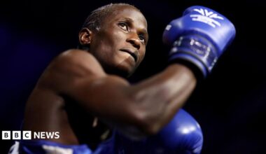 Nuhu Batte, with blue boxing gloves on and with an arm flexed, preparing to fight.