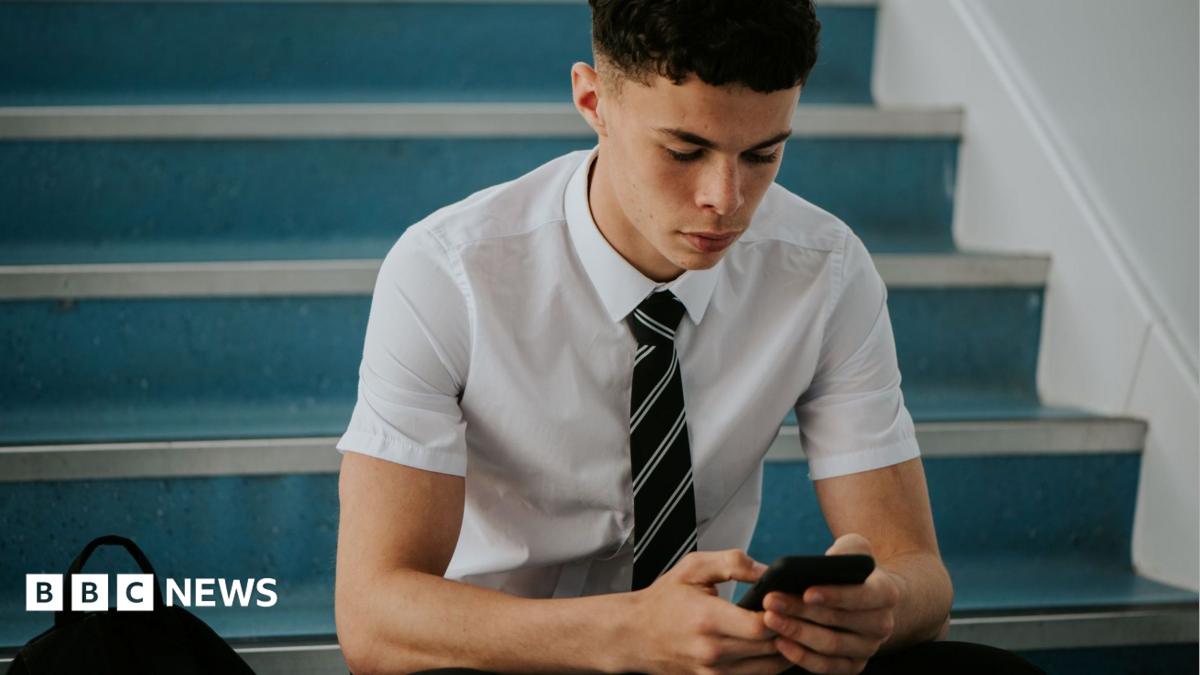 an adolescent boy in a short-sleeved shirt and a tie sitting on stairs, looking at a phone