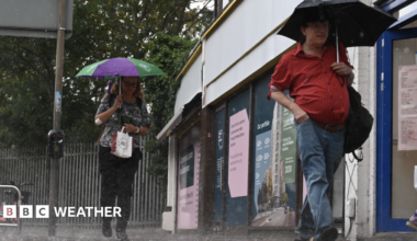A man and a woman walk through torrential rain while holding umbrellas