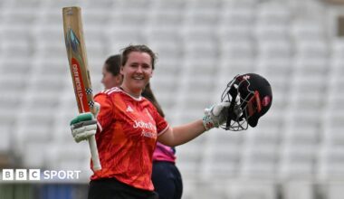 Kathryn Bryce raises her bat as she celebrates her century