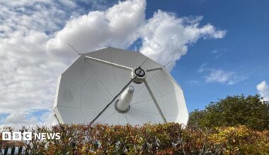 A large white satellite is pointing up to blue skies.