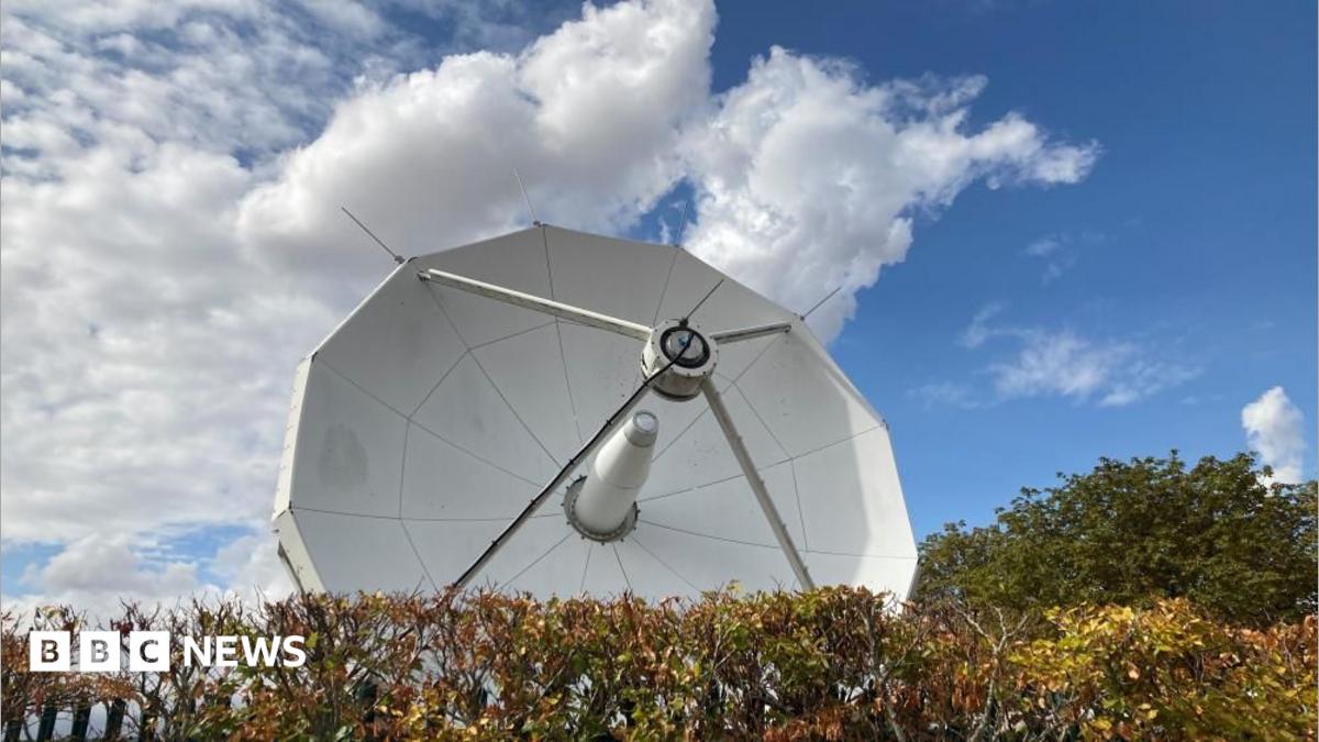 A large white satellite is pointing up to blue skies.