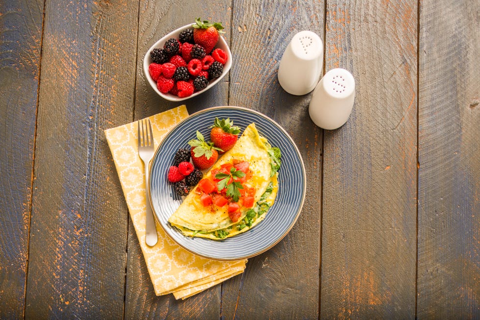 Breakfast on table Omelette with tomatoes and greens beside a bowl of berries on a wooden table