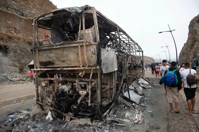 People walk past a bus which was burned during clashes between police and people attempting to cross from Morocco