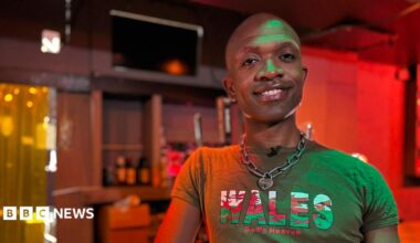 Bald man smiles at camera. He is wearing a green t-shirt with the Welsh flag on the word 'Wales, God's Heaven'