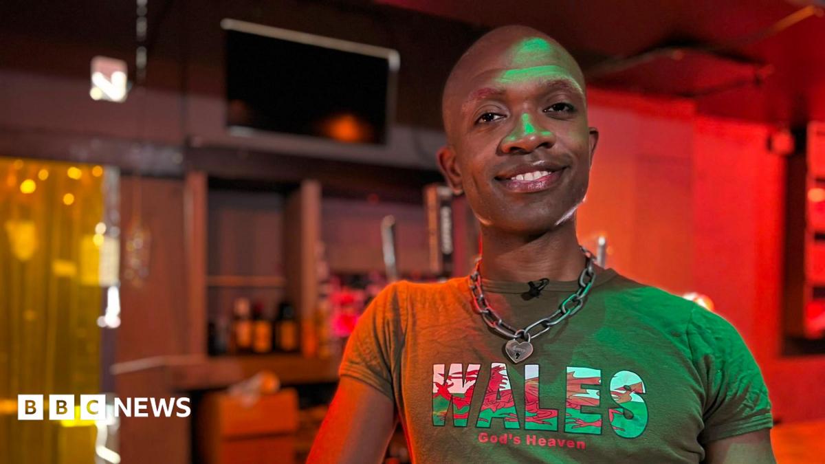 Bald man smiles at camera. He is wearing a green t-shirt with the Welsh flag on the word 'Wales, God's Heaven'