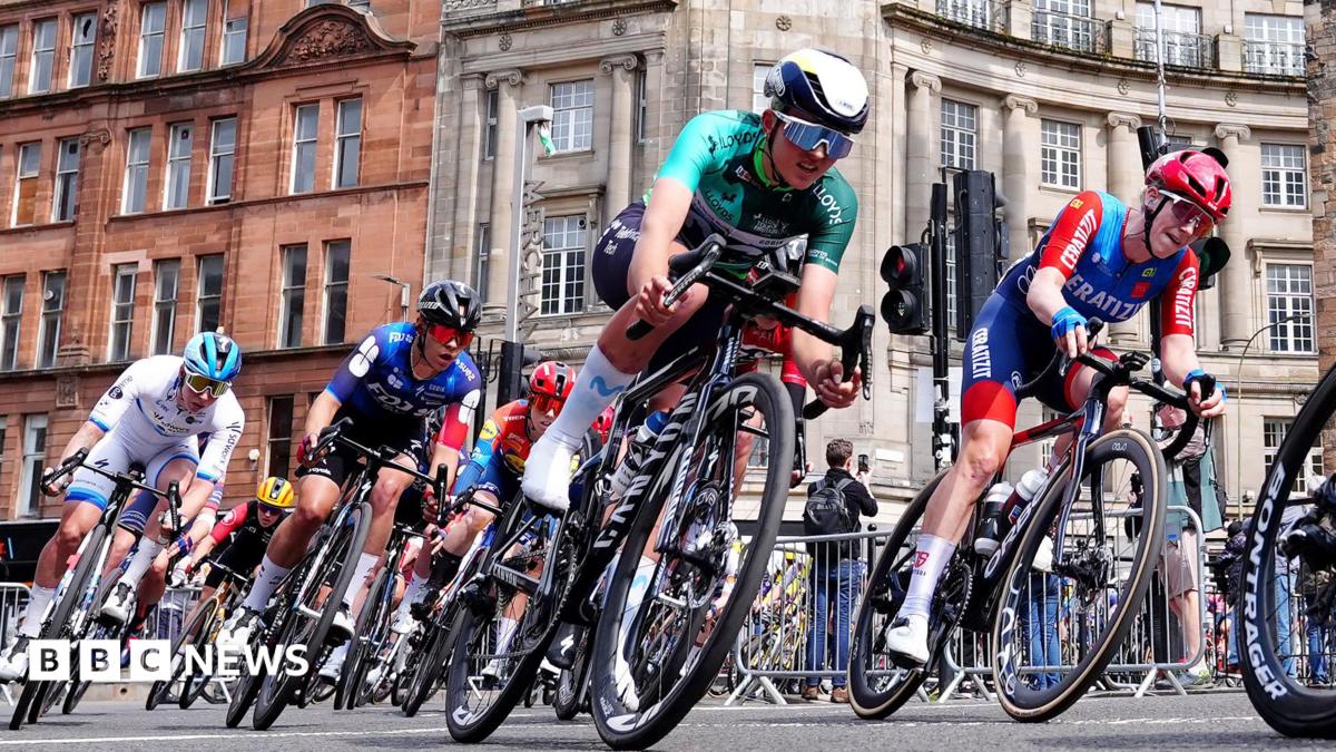 A number of cyclists wearing different coloured outfits, ride past during a race held on the streets of a city.