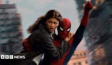 Spider-Man swings through the city on web whilst holding MJ, played by Zendaya.