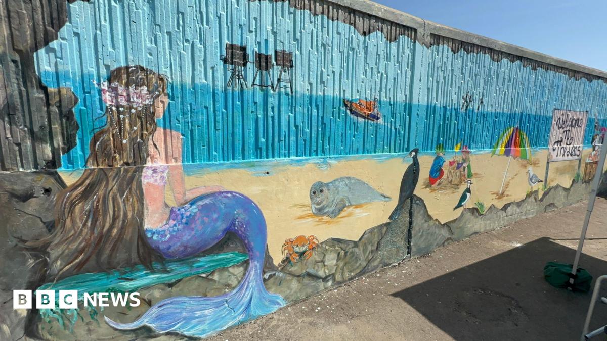 A seafront mural featuring a mermaid, seal, crab, boat and children playing in sand.