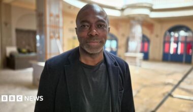 A picture of Bayo Alaba, standing indoors and wearing a black jacket and black t-shirt