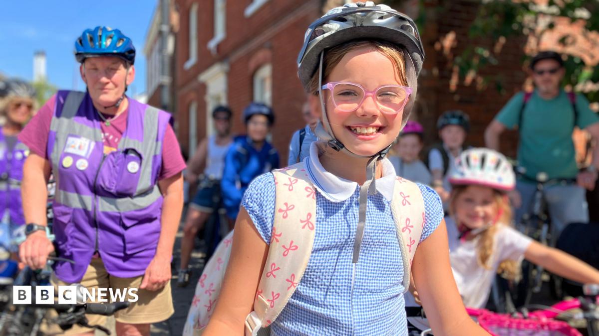 A girl with a bike helmet and school rucksack with others on bikes in the background.