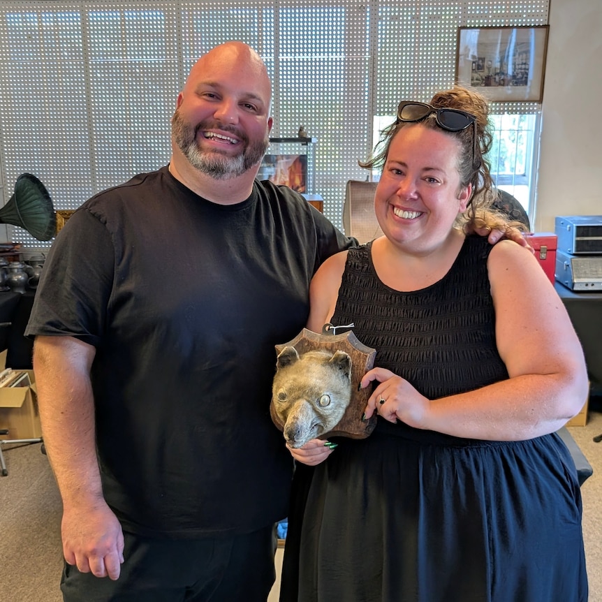 A man and a woman hold a mounted taxidermy animal head that resembles a thylacine, or Tasmanian tiger.