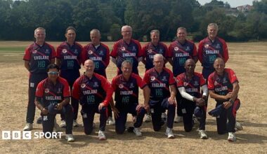 The 2026 England Over-60s World Cup squad looking towards the camera with barren grass in the foreground and green trees in the background.