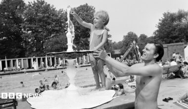 A black and white photo of a dad holding up his son so he can touch a water fountain at Malvern Park in Solihull, in 1976.