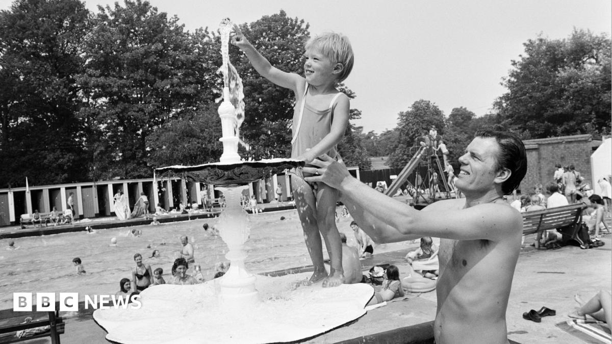 A black and white photo of a dad holding up his son so he can touch a water fountain at Malvern Park in Solihull, in 1976.