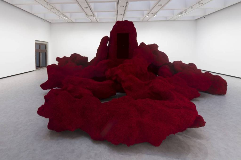a large red sculpture that sprawls around a room with sharp, but organic, lines that almost look like limbs of a building