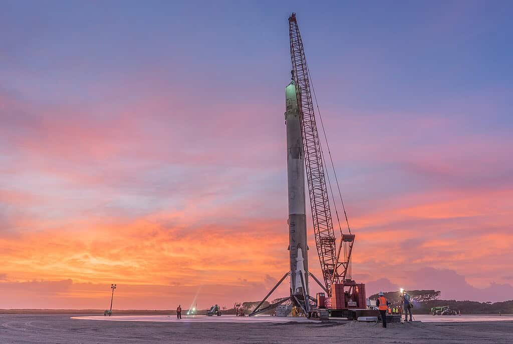 Crane holding up a part of a rocket in an open empty landscape with vivid a sunset in the background