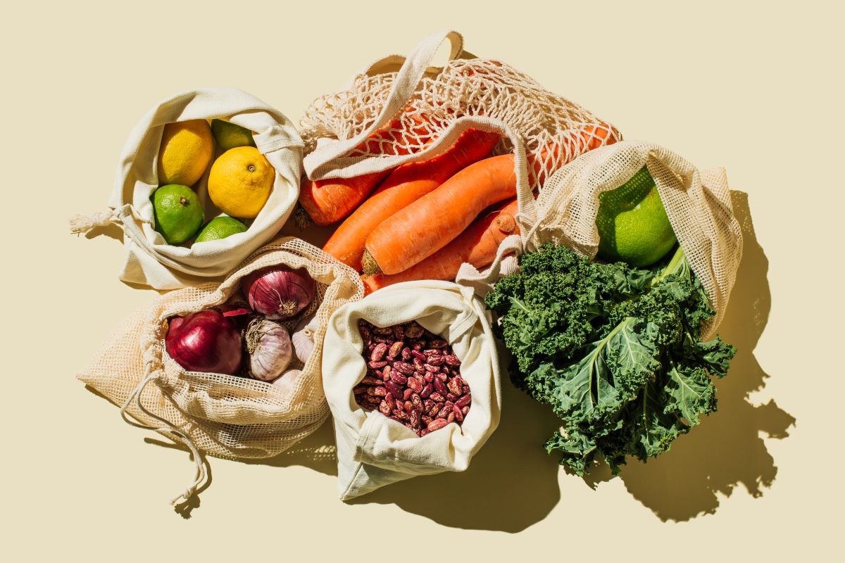 Variety Fresh of organic fruits and vegetables and healthy vegan meal ingredients in reusable eco cotton bags on beige background . Zero waste shopping concept. Healthy food, clean eating, eco friendly, no plastic. Flat lay, top view - stock photo